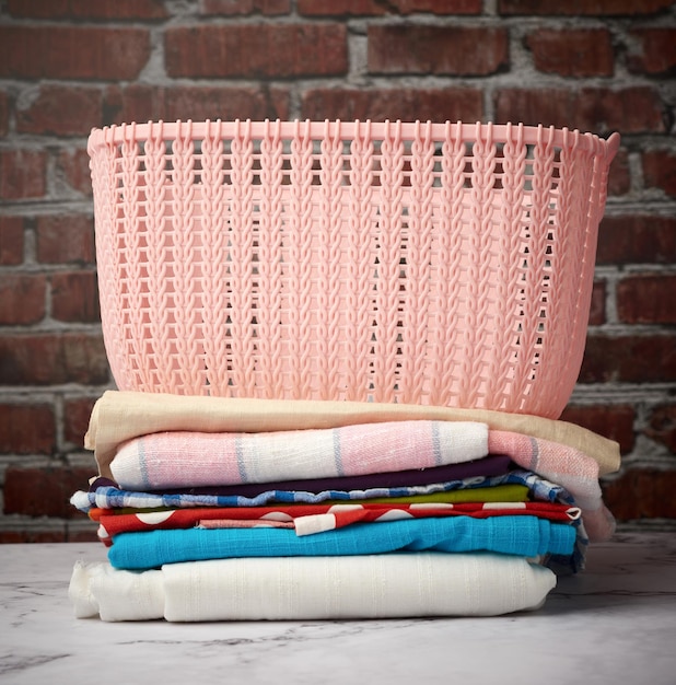 Photo stack of folded laundry and empty laundry basket brown brick wall background close up