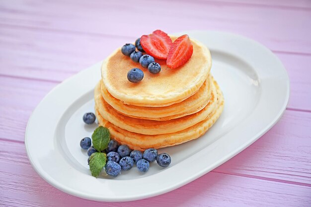 Stack of fresh pancakes with berries on wooden background