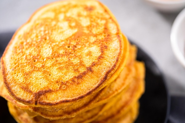 Stack of fresh pumpkin pancakes on a black plate.