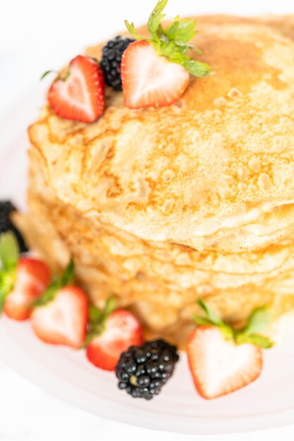 Stack of freshly baked crepes with berries on a cake stand.