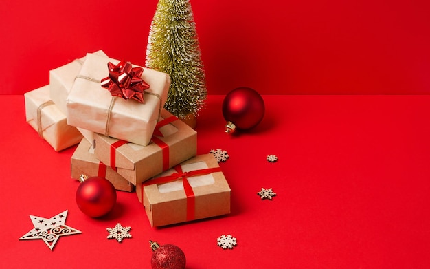 A stack of gifts in kraft paper and kraft boxes on a red background with wooden eco decorations