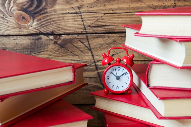 A stack of hardcover books and an alarm clock on a wooden table. Copy space for text