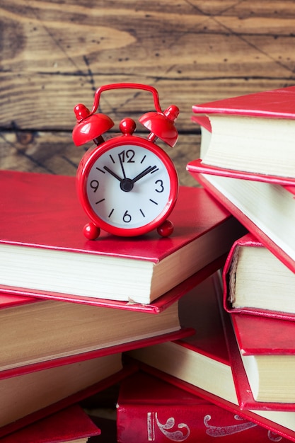 A stack of hardcover books and an alarm clock on a wooden table. Copy space for text