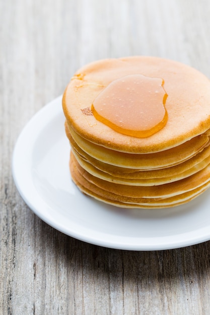 Stack of homemade pancakes with honey on wooden table.