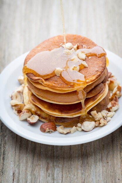 Stack of homemade pancakes with honey on wooden table.