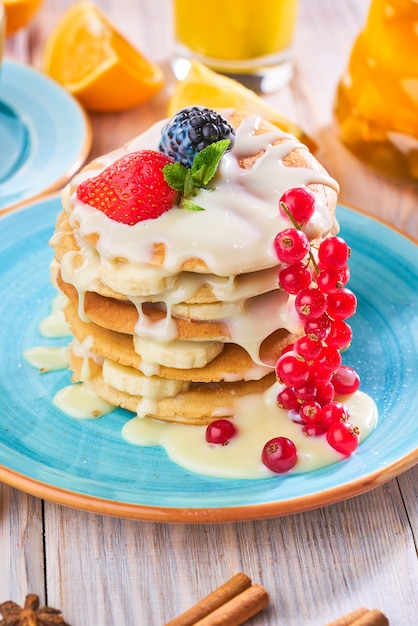 Stack of homemade pancakes with strawberrie, banana and red currant on a blue plate