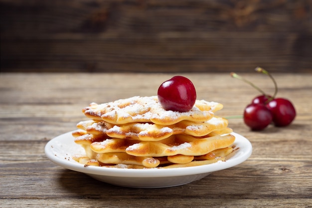 Stack of homemade waffles with cherries on wooden table.