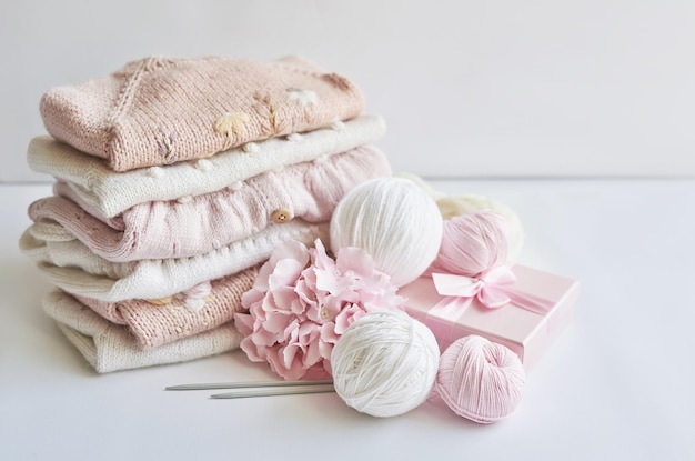 Stack of knitted clothes and balls of yarn knitting needles\
accessories for knitting baby clothes needlework hobby knitting\
handwork