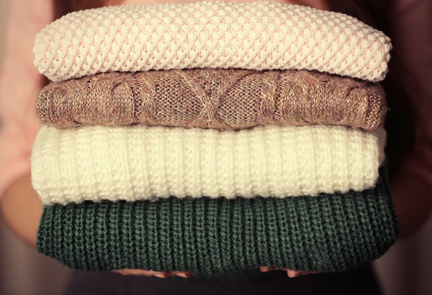 Stack of knitted clothes in female hands closeup