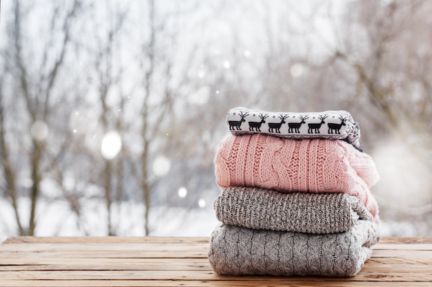 Stack of knitted clothes on wooden table on winter nature ourdoor