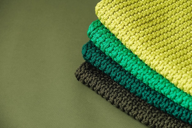 Стопка вязаного материала из ниток желто-зеленого коричневого цвета на зеленом фоне