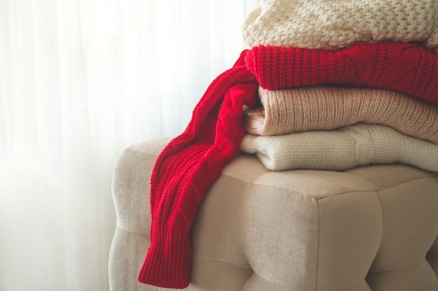 A stack of knitted sweaters in the interior of the living room. The concept of autumn winter comfort