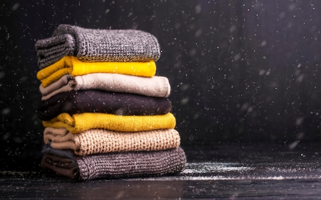 a stack of knitted winter sweaters in several shades of yellow on black background falling snow