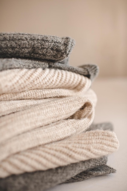 Stack of knitted wool textile sweaters clothes on white blanket in bed at home room close up Winter cozy season