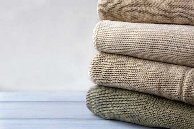 Stack of knitted woolen sweaters on light wooden table. 