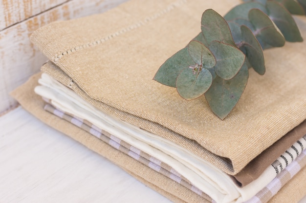 Stack of linen and cotton kitchen towels on white wood kitchen table with branch of eucalyptus