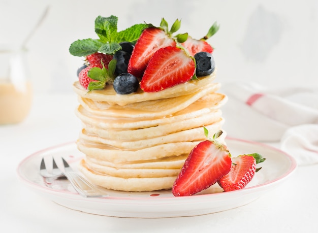 Stack of  little pancakes with honey, fresh strawberries and sauce on light wooden background.