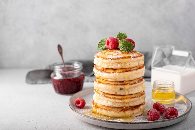 A stack of lush pancakes with raspberries and honey on a gray plate