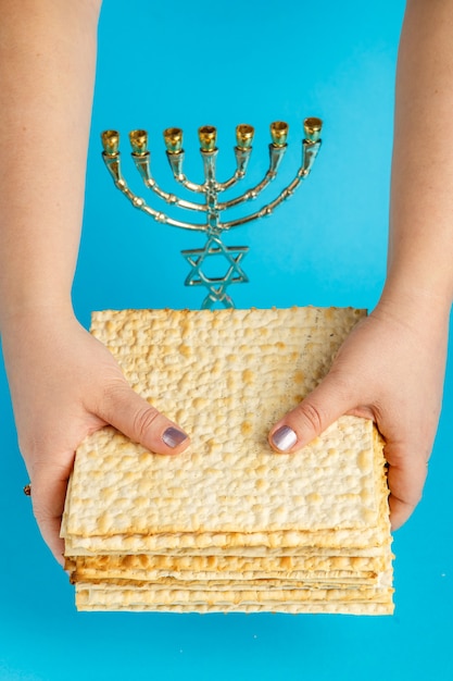 A stack of matzo in female hands on a blue surface near the menorah