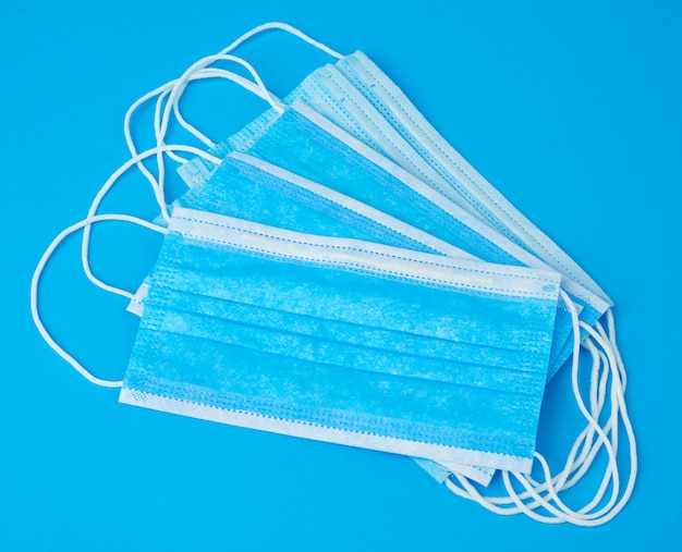 Stack of medical masks made of non-woven material with white rubber bands on a blue background