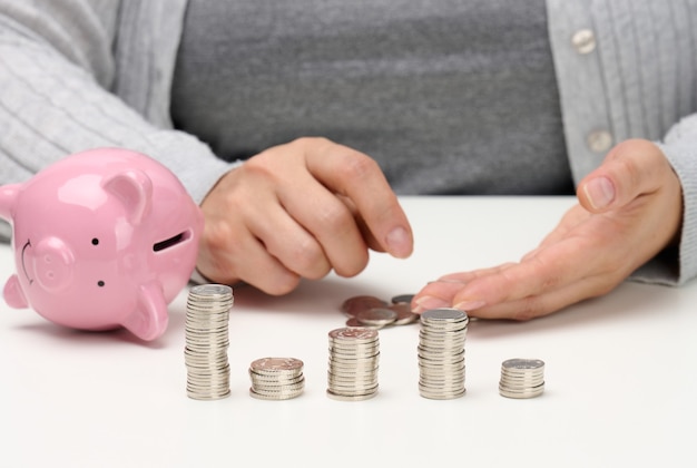 Stack of metal coins and a ceramic pink piggy bank. Man counting money, poverty concept, budget planning