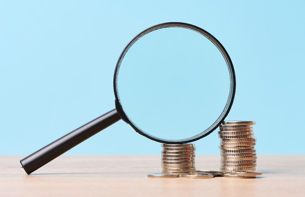 A stack of metal coins and a plastic magnifier on a blue background The concept of increasing taxes subsidies