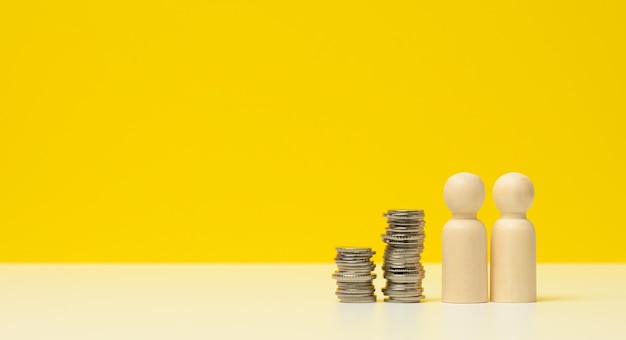 Stack of metal coins and wooden figures of men on a white
table. savings and expenses, family budget, subsidies from the
state, copy space