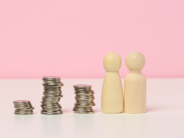 A stack of metal coins and wooden figures of men on a white table. Savings and expenses, family budget, subsidies from the state