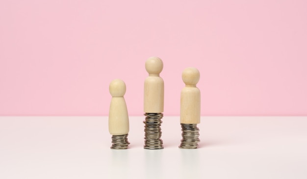 A stack of metal coins and wooden figures of men on a white table. Savings and expenses, family budget, subsidies from the state