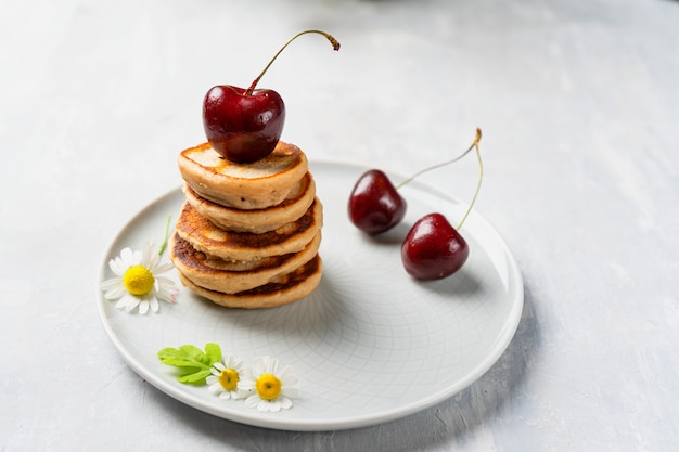 A stack of mini pancakes, in a plate with cherries