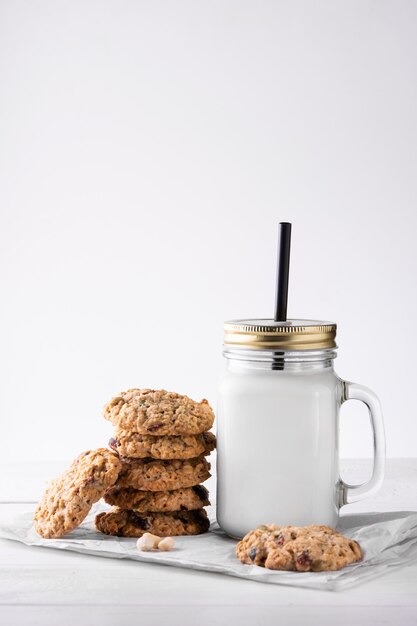 A stack of oatmeal cookies and a mug of milk on a light wall. Close-up.