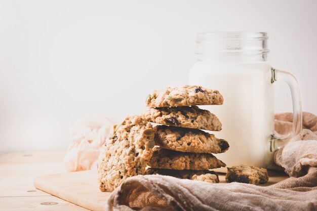 A stack of oatmeal cookies and a mug of milk on a light wall. Close-up.