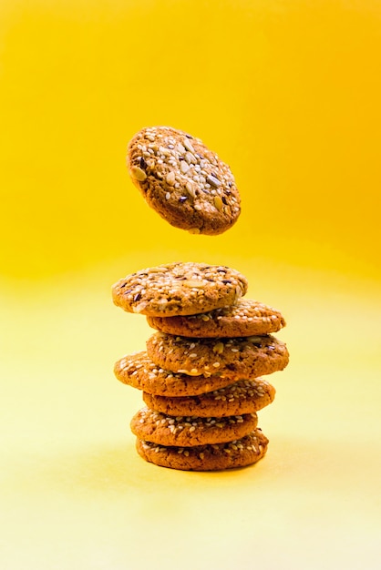 Stack of oatmeal cookies with levitating cookie on yellow