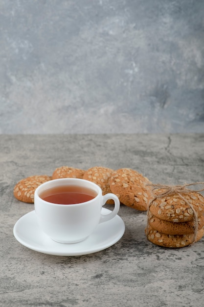 Stack of oatmeal cookies with seeds and cup of tea on stone.