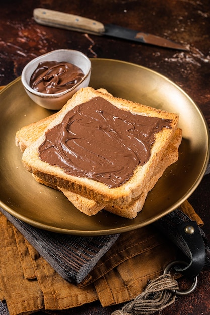 写真 プレートにチョコレートヘーゼルナッツクリームを入れたトーストのスタック。暗い背景。上面図。