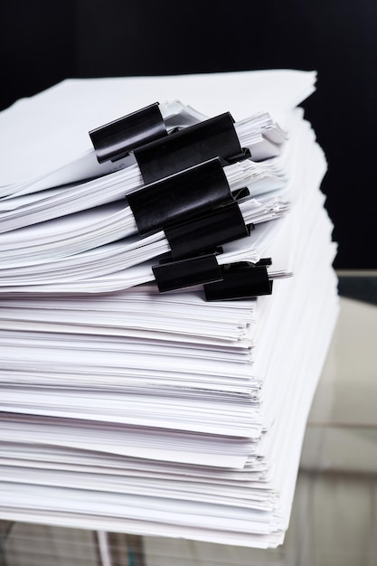 A stack of office papers some of which are fastened with black binders