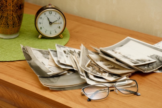 안경과 알람 시계 메모리가 있는 탁자 위에 흩어져 있는 오래된 흑백 사진 더미
