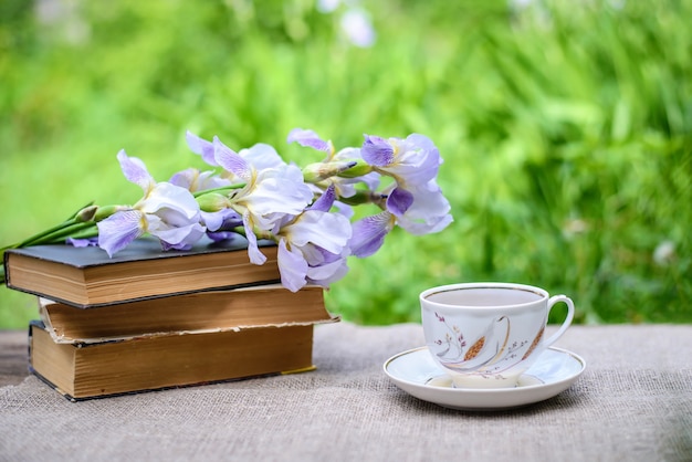 古い本のスタック、紫色の花の菖蒲とお茶のカップ