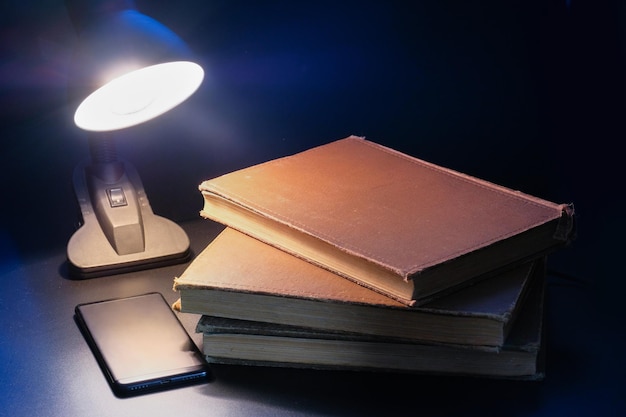 A stack of old books and table lamp on a dark background