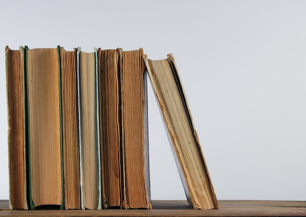 Stack of old books on woden shelf against the a white wall