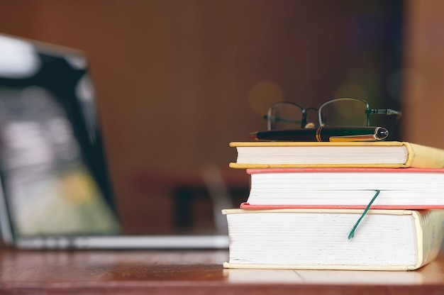 Stack of old boos on wooden table with laptop in library.