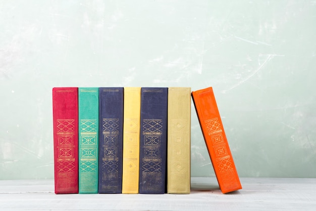 A stack of old colored books on shelf and green background