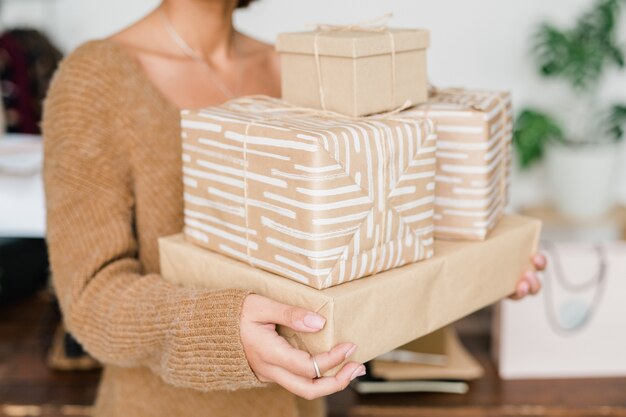 Foto pila di scatole regalo confezionate e avvolte detenute da giovane donna casual in pullover lavorato a maglia beige