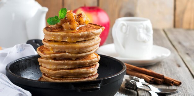 Stack of pancakes from buckwheat flour with baked apples and cinnamon on old wooden background. A healthy breakfast. Selective focus.