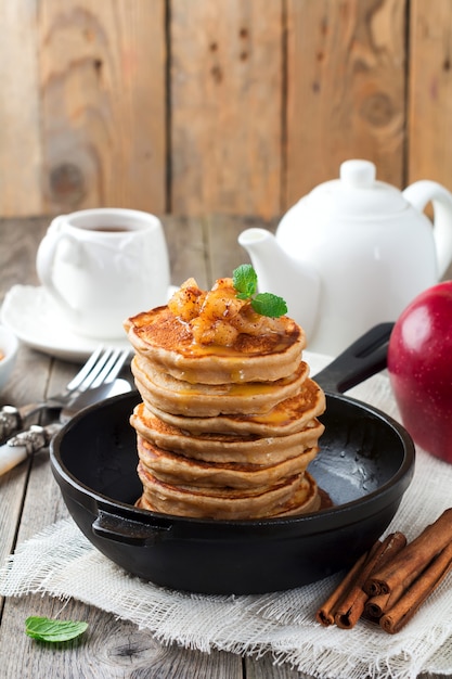 Stack of pancakes from buckwheat flour with baked apples and cinnamon on old wooden surface.Selective focus.