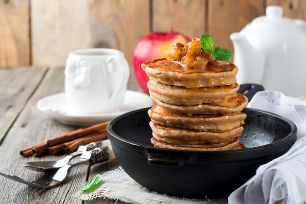 Stack of pancakes from buckwheat flour with baked apples and cinnamon on old wooden surface.Selective focus.