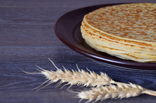 A stack of pancakes on a plate.Two ears of wheat next to the plate.Traditional Russian food.