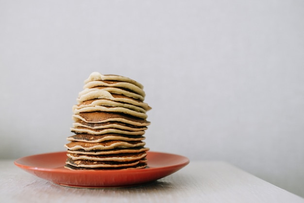 Stack of pancakes  in red plate on table on gray wall background