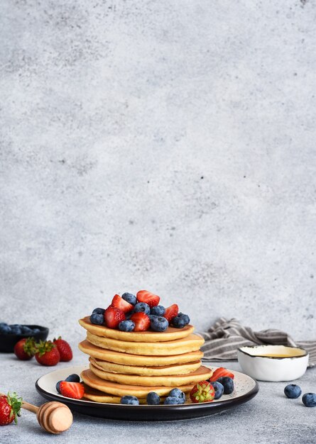 Stack of pancakes with berries and honey
on a concrete background.