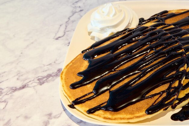 Stack of pancakes with chocolate syrup and whipped cream on a white plate